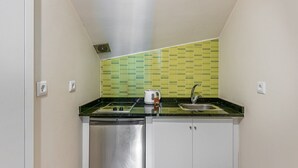 Une cuisine compacte avec un crédence recouverte de carreaux verts, un évier en acier inoxydable et un lave-vaisselle.