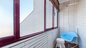 Un balcon étroit avec une chaise bleue, une petite table ronde et une fenêtre à cadre rouge.