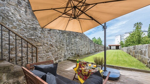 A patio with a wooden bench and table, stone walls, and a grassy lawn.