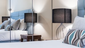 A modern hotel room with a large bed, a bedside table, a lamp, and a mirror.