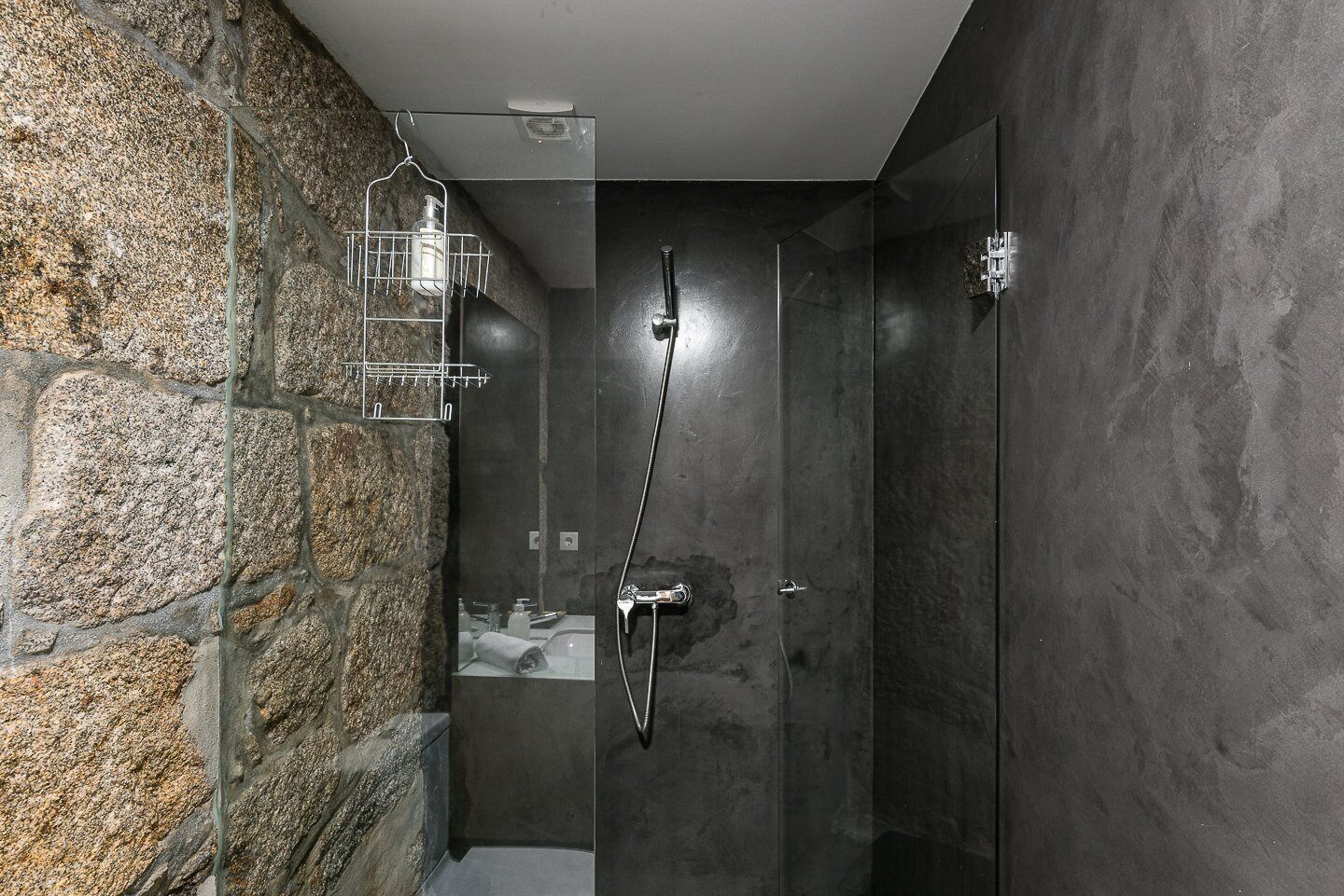 A modern bathroom with a stone wall, a glass shower enclosure, and a visible towel rack.