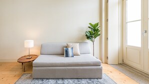 Un saló modern amb un sofà gris, una taula auxiliar petita amb una làmpada i una planta verda gran.