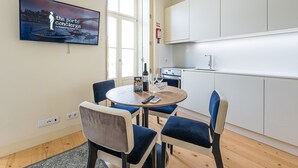 Una cuina moderna amb armaris blancs, una taula de dinar amb quatre cadires i un televisor que mostra una vista panoràmica.