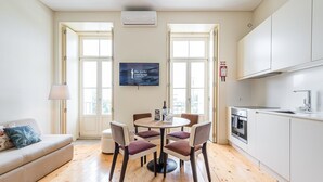 Una cocina moderna con armarios blancos, un área de comedor con una mesa redonda y cuatro sillas, y un sofá con una lámpara.