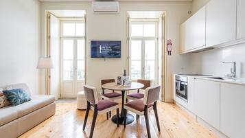 Una cucina moderna con pensili bianchi, un'area pranzo con un tavolo rotondo e quattro sedie, e un divano con una lampada.