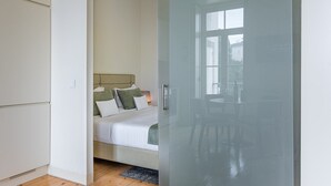 Un dormitorio con cama, mesita de noche y ventana.