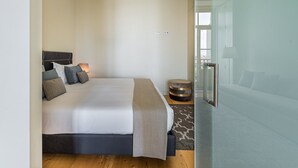 A modern bedroom with a large bed, bedside lamps, a round side table, and a glass door leading to a balcony. - GuestReady - La Maison Aires Gouveia 5 (Porto)
