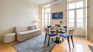 A living room with a sofa, a dining table with chairs, a TV, and a window with a view. - GuestReady - La Maison Aires Gouveia 5 (Porto)