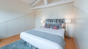 Un dormitorio con cama, dos lámparas de noche, cabecero con diseño texturizado y suelo de madera.