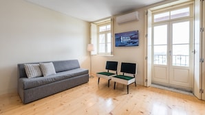 Una sala de estar moderna con un sofá gris, dos sillones verdes, un televisor de pantalla plana y una ventana con vistas.