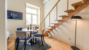 A modern room with a wooden staircase, a round table with chairs, and a large window. - GuestReady - La Maison Aires Gouveia #8 (Porto)