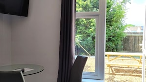 Een kamer met een eenpersoonsbed, een klein tafeltje met een stoel, een aan de muur bevestigde televisie en een raam met gordijnen.