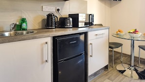 Een moderne keuken met een inbouwvaatwasser, koffiezetapparaat en magnetron. Er staat een glazen tafel met twee stoelen en een kom met fruit.