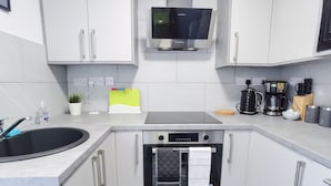 Een moderne keuken met witte kasten, een inbouwoven, een magnetron en een koffiezetapparaat.