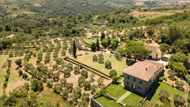 Vista aérea de una finca de campo con una construcción grande, jardines ajardinados y campos circundantes.