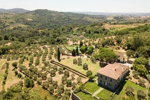 Vue aérienne d’un domaine rural comprenant un grand bâtiment, des jardins aménagés et des champs environnants.