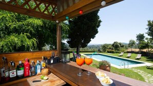 Zona de bar con vistas a la piscina, mesas al aire libre y diferentes botellas.