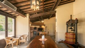 Un comedor rústico con una mesa de madera, sillas de mimbre y un prensador antiguo.