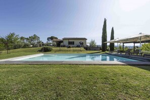 Une piscine avec une terrasse en bois, une maison en arrière-plan et un ciel dégagé.