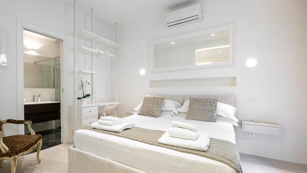 Una habitación de hotel moderna con una cama grande, un tocador con espejo, una silla y un equipo de aire acondicionado.