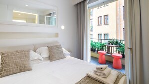 Una habitación de hotel con cama, espejo, balcón con taburetes rojos y vistas a edificios.