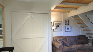 Un salón acogedor con un gran puerta estilo establo blanca, un sofá de cuero marrón y una escalera que sube a un nivel superior.