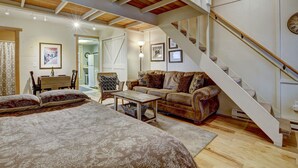 Un salón espacioso con una cama grande, una mesa de centro de madera, un sofá de cuero y una escalera con barandilla de madera.