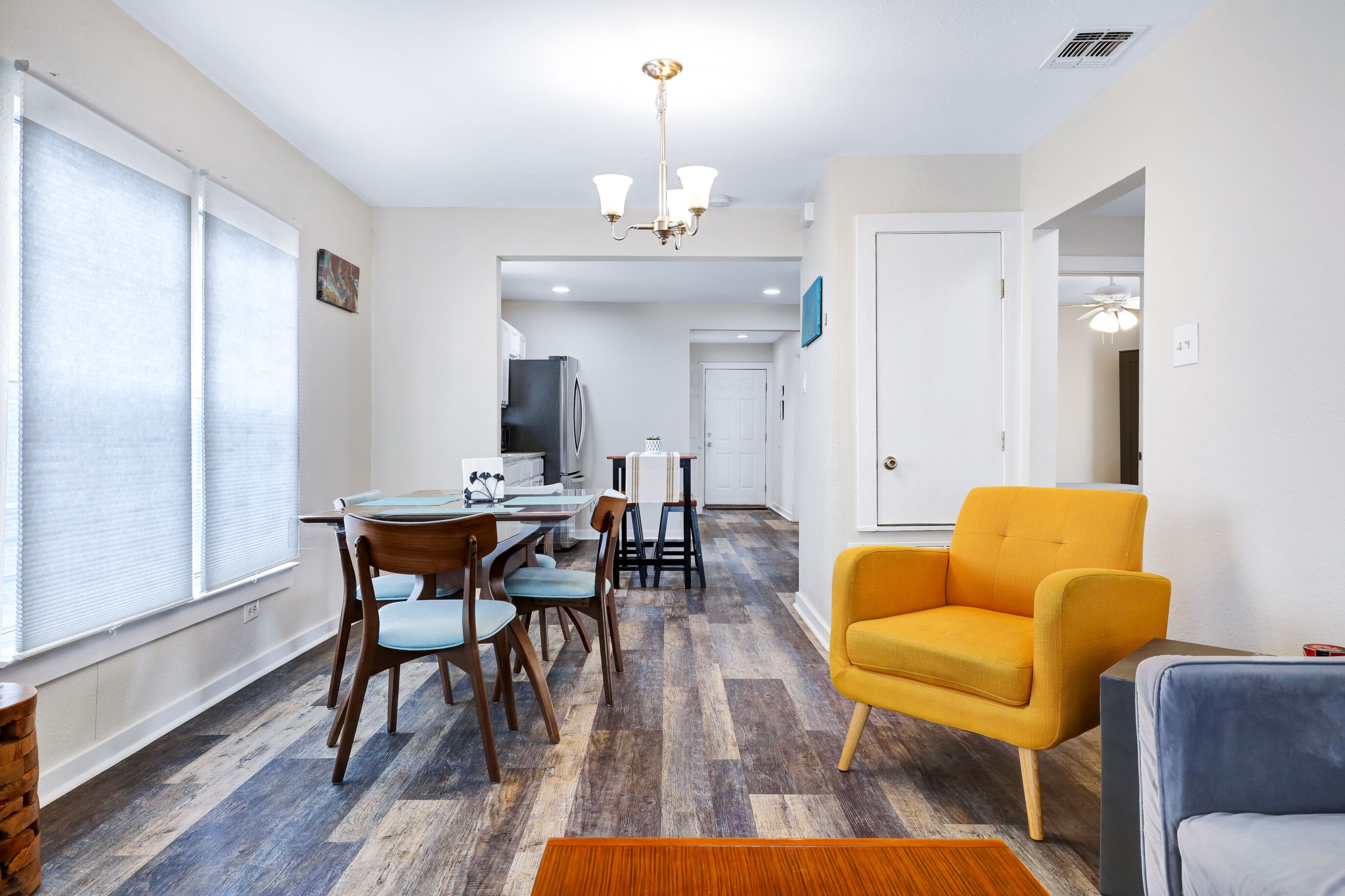 A modern living room with a dining area, a yellow armchair, and a blue sofa.