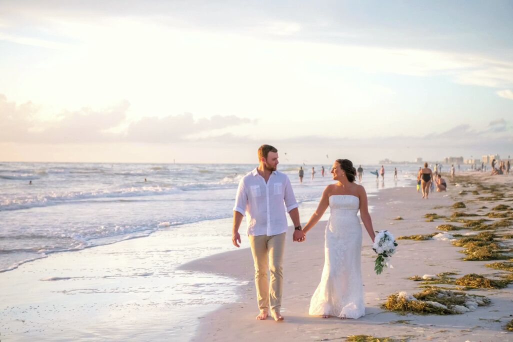 A couple walking hand in hand on a beach with the ocean in the background.