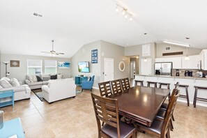A spacious living area with a large dining table, a sofa, and a kitchen in the background. - Latitude Adjustment | Poolside Paradise (Port Aransas)