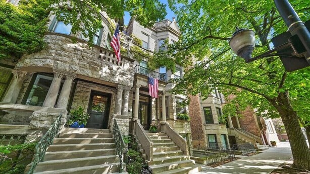 A historic building with a stone facade, multiple American flags, and a set of stone steps leading to the entrance.