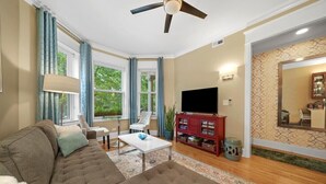 A living room with a sofa, armchairs, a coffee table, a TV, and a ceiling fan.
