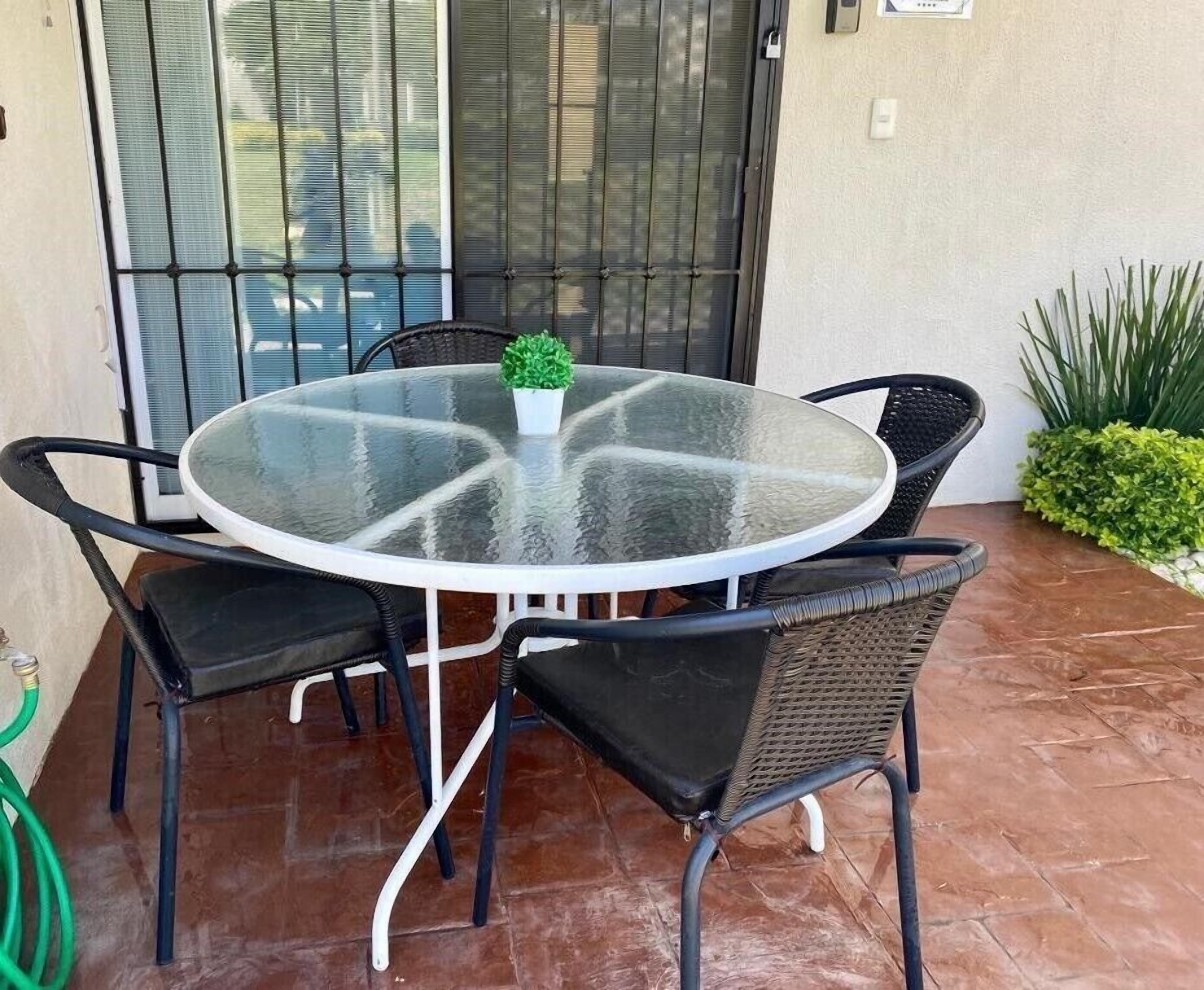 A round glass table with a white frame, surrounded by four black wicker chairs with cushioned seats.