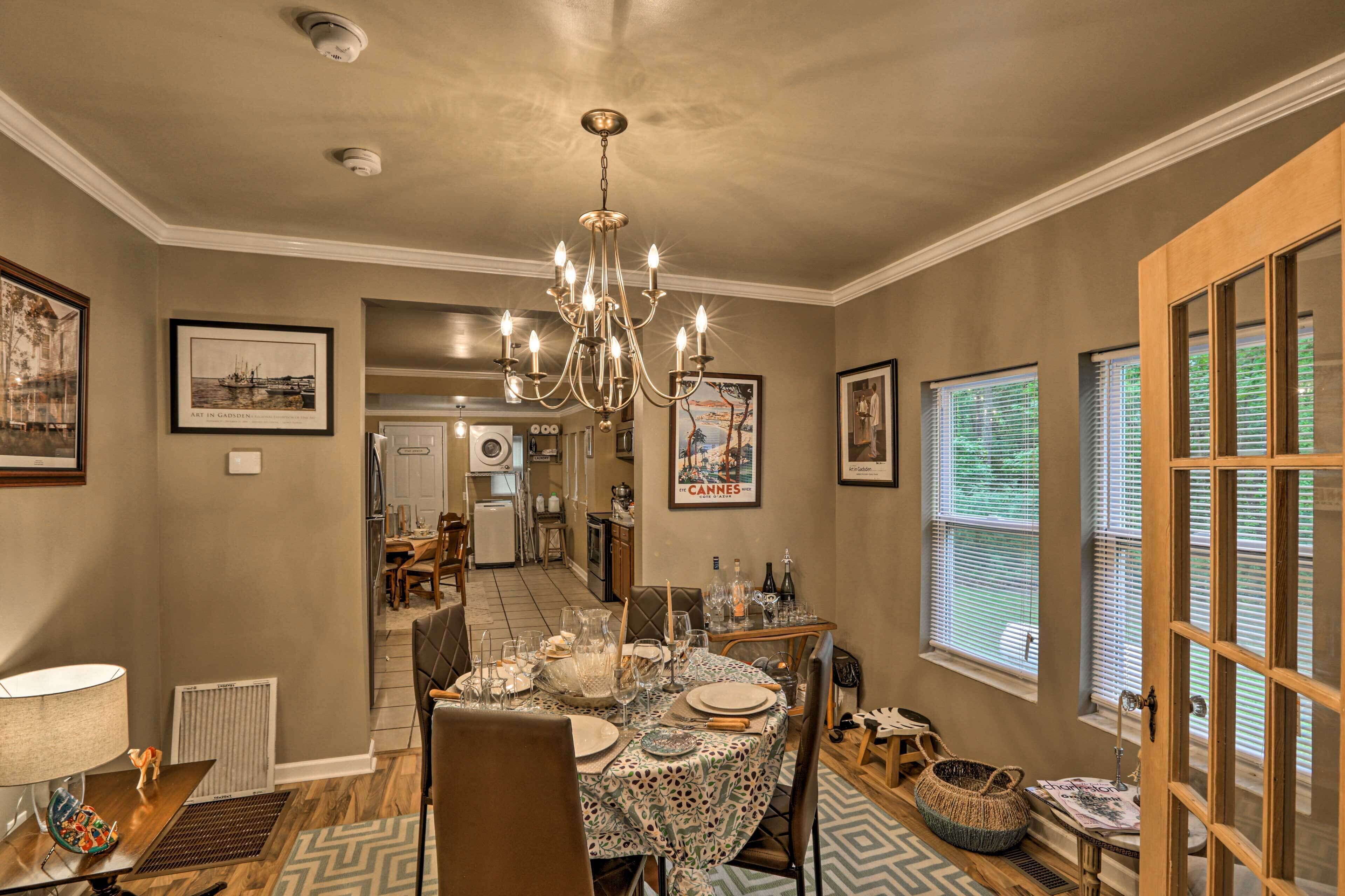 A dining area with a chandelier, framed artwork, and a view of the kitchen.