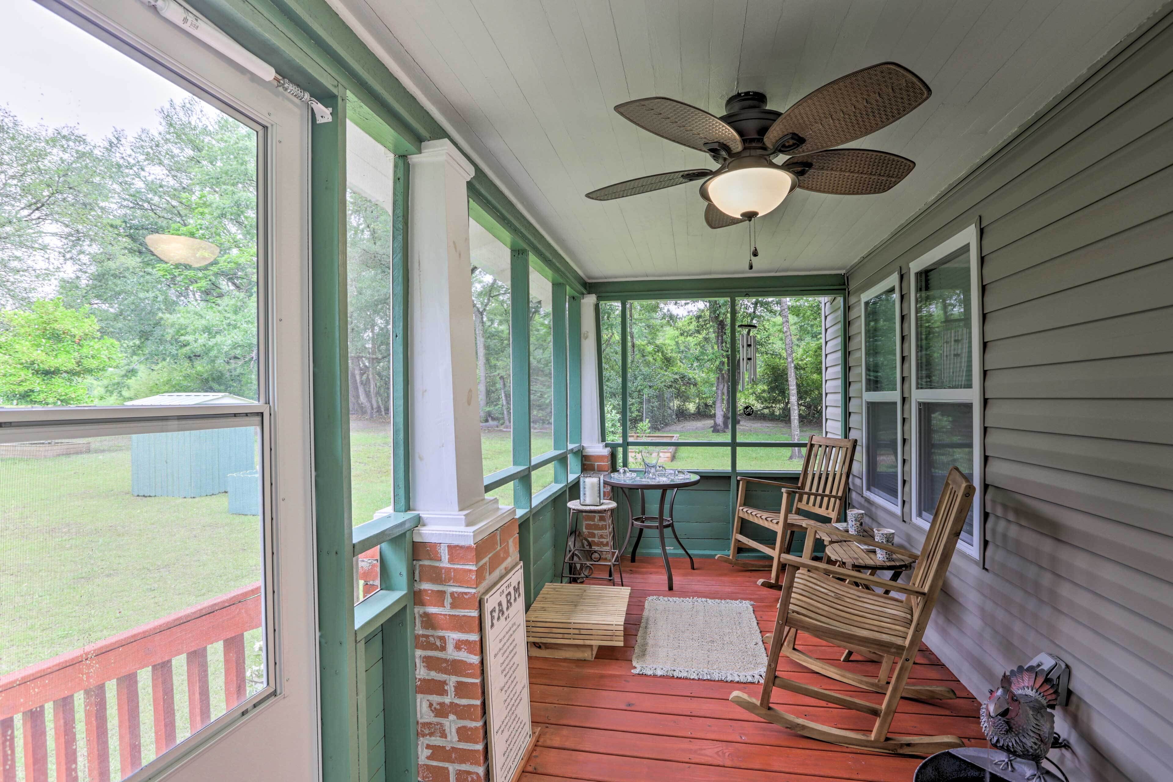 A covered porch with a ceiling fan, rocking chairs, a small table, and a view of the backyard.