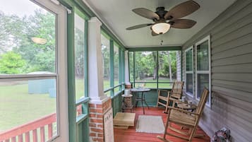 A covered porch with a ceiling fan, rocking chairs, a small table, and a view of the backyard.