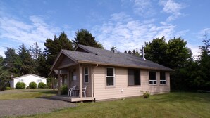 A single-story house with a front porch, a small attached garage, and a well-maintained lawn. - In the Heart of Netarts (Tillamook)