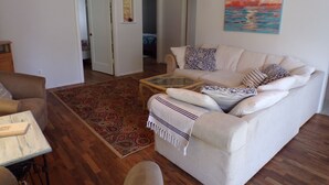 A living room with a beige sofa, patterned rug, and a glass coffee table. - In the Heart of Netarts (Tillamook)