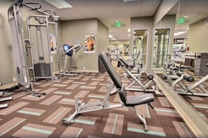 A gym with various exercise equipment, a mirrored wall, and a patterned carpet.