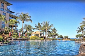 A resort pool area with palm trees, a small gazebo, and a building with balconies.