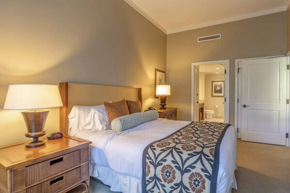 A hotel room with a bed, bedside lamps, a nightstand, and a door leading to a bathroom.