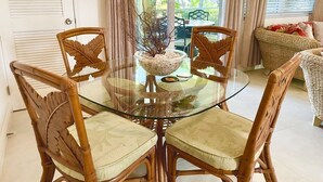 A glass-top dining table with four wicker chairs, a decorative centerpiece, and a view of the outdoors through large windows. - Villa Diez, Pool & Boat Charters (Grace Bay)