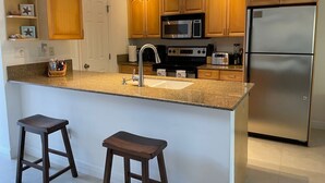 A kitchen with wooden cabinets, a stainless steel refrigerator, a microwave, a stove, and two bar stools. - Villa Diez, Pool & Boat Charters (Grace Bay)