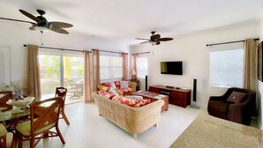 A spacious living room with a sofa, dining table, chairs, ceiling fans, and a TV. - Villa Diez, Pool & Boat Charters (Grace Bay)