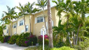 A two-story building with a yellow facade, white shutters, and a well-maintained garden with palm trees and flowering plants. - Villa Diez, Pool & Boat Charters (Grace Bay)