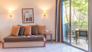 A room with a bed, two wall-mounted lamps, a framed picture, and a view of an outdoor patio with chairs and a table. - Studio Cosy et Abordable avec Wi-Fi Gratuit (Grospierres)