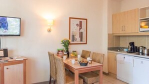 A compact kitchen with a dining area, a television, and a framed picture on the wall. - Studio Abordable avec Climatisation | Wi-Fi (Grospierres)