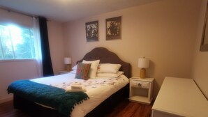 Un lit bien fait, recouvert d’une couvre-lit à motifs floraux, une table de chevet avec une lampe et une petite armoire.