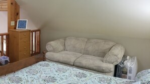 Un dormitorio con una cama litera, una escalera de madera, un pequeño aparador de madera y una colcha estampada.