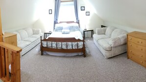 Un dormitorio con cama de madera, dos sofás blancos, un aparador de madera y una mesita.